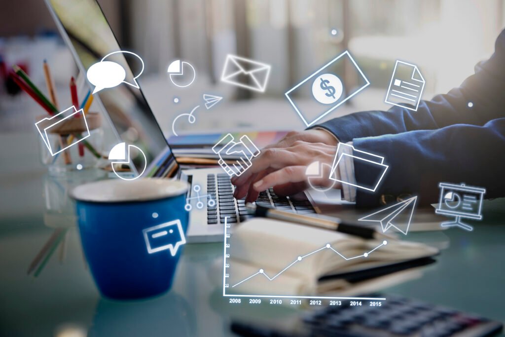 Businessperson typing on laptop with digital marketing and analytics icons overlayed, including graphs, charts, messages, and folders on a desk with coffee and stationery.